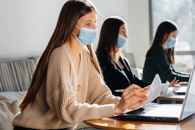 Un groupe de filles masquées garde une distance sociale dans un café lorsqu'elles travaillent sur des ordinateurs portables.