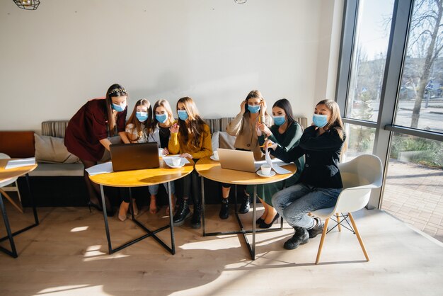 Un groupe de filles masquées s'assied dans un café et travaille sur des ordinateurs portables