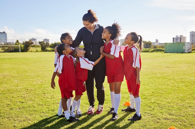 Groupe de football féminin et terrain avec entraîneur team building câlin et solidarité à l'entraînement sportif Diversité sportive des enfants féminins et heureux avec le travail d'équipe d'amis et l'entraînement de football avec une femme mentor