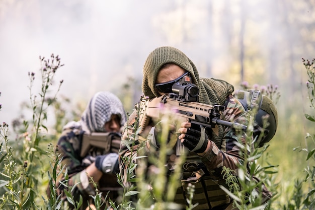 Groupe de force de l'armée se déplaçant avec des fusils à travers l'herbe haute dans la forêt tout en effectuant une action militaire coordonnée