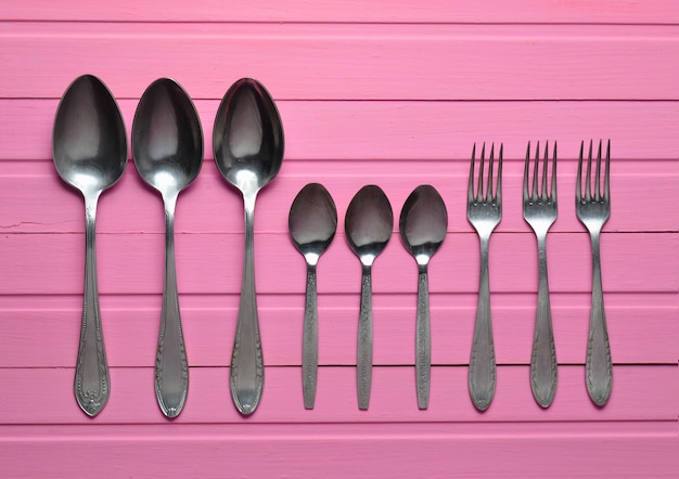 Un groupe de fourchettes, une cuillère sur une table en bois rose. Coutellerie. Vue de dessus.