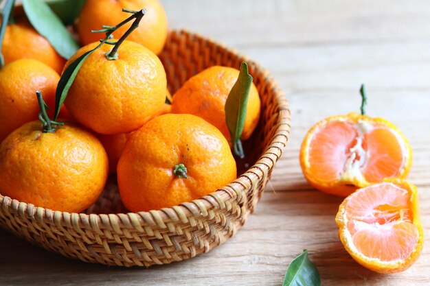 Groupe de fruits frais de mandarines avec des feuilles dans le panier en rotin sur la table en bois