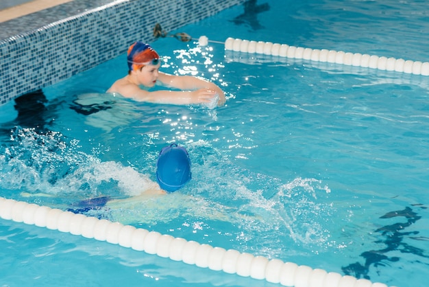 Un groupe de garçons et de filles s'entraîne et apprend à nager dans la piscine avec un instructeur. Développement des sports pour enfants.