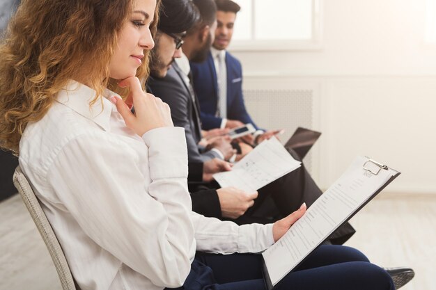 Groupe de gens d'affaires assis sur des chaises. Candidats au chômage en attente d'un entretien, assis au bureau de l'employeur et remplissant le questionnaire, espace de copie