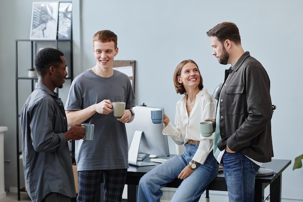 Groupe de gens d'affaires buvant du café dans des tasses et se parlant pendant la pause-café au bureau