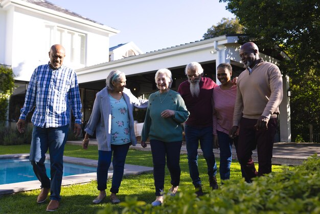 Photo un groupe heureux et diversifié d'amis âgés marchant à côté de la piscine dans un jardin ensoleillé