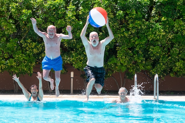 Groupe heureux de personnes mûres appréciant l'été et la piscine sautant et jouant avec le bal