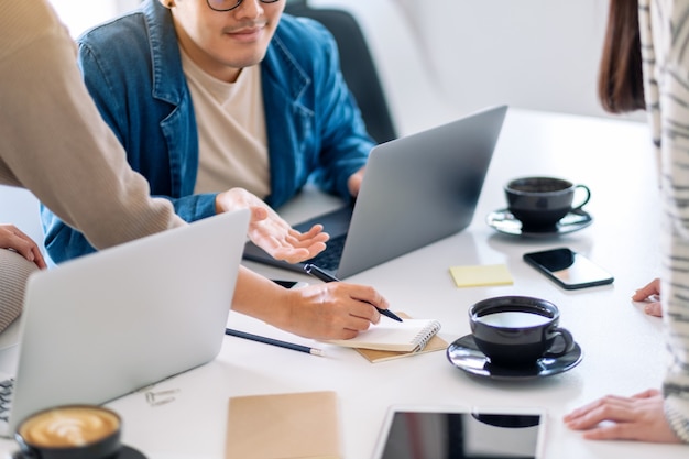 Groupe d'hommes d'affaires utilisant un ordinateur portable tout en discutant et en écrivant sur un ordinateur portable sur la table au bureau