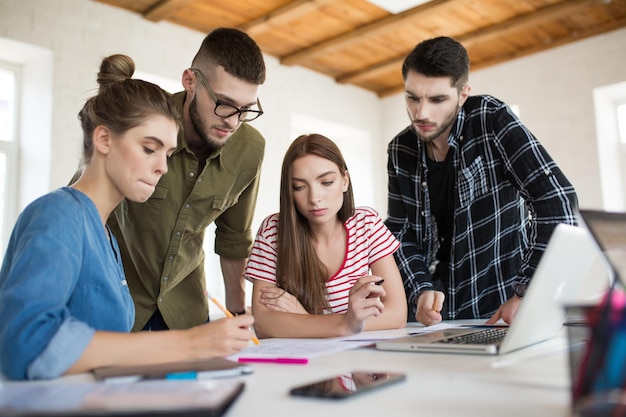 Groupe d'hommes et de femmes d'affaires travaillant pensivement avec des croquis tout en passant du temps au travail Jeunes créant un nouveau projet ensemble dans un bureau moderne