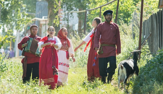 Groupe d'hommes et de femmes en costumes folkloriques russes dans la nature chantant la célébration