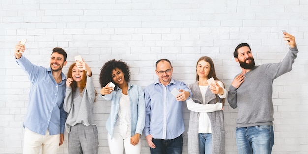 Un groupe d'hommes et de femmes heureux et souriants prenant un selfie.