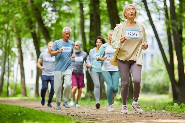 Photo groupe d'hommes et de femmes seniors actifs modernes passer du temps ensemble dans le parc marathon, plan large