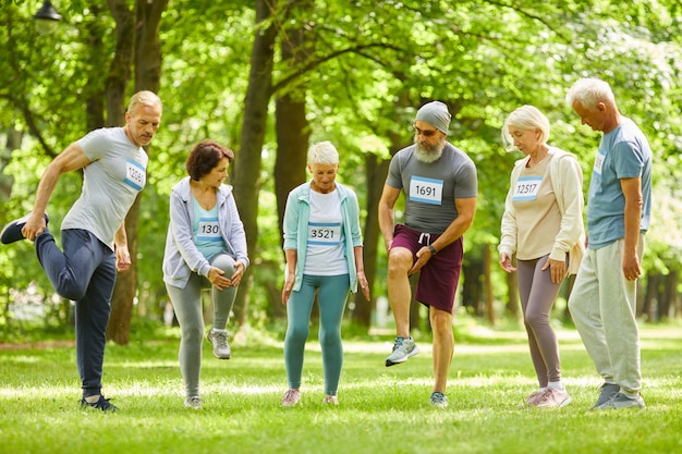 Groupe d'hommes et de femmes seniors participant à la formation marathon qui s'étend des jambes juste avant de courir dans le parc
