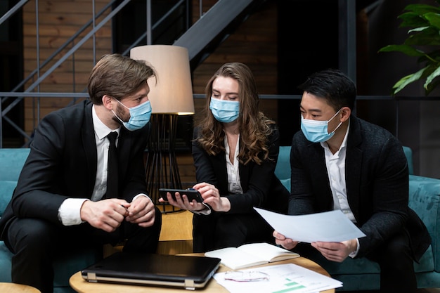 Groupe d'hommes et de femmes tenir une réunion d'affaires près d'un ordinateur portable portant des masques médicaux de protection sur le visage dans la salle de conférence
