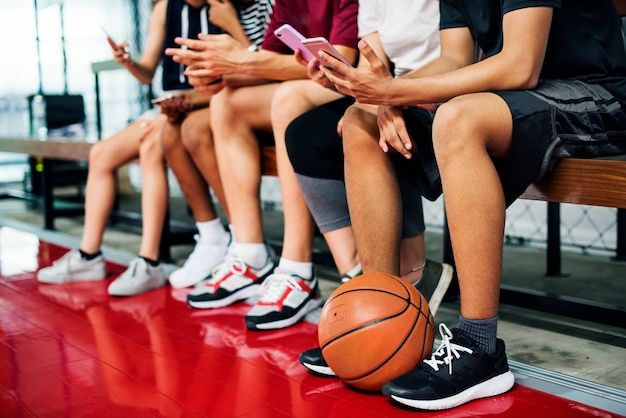 Groupe de jeunes amis adolescents sur un terrain de basket relaxant à l&#39;aide de smartphone