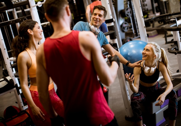 Groupe de jeunes amis discutant et riant assis sur le sol du gymnase après l&#39;entraînement