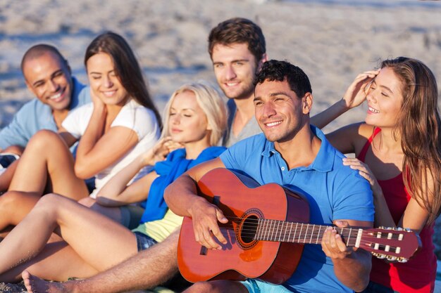 Groupe de jeunes amis heureux sur la plage avec guitare