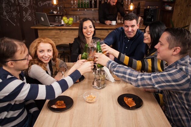 Groupe de jeunes amis heureux portant un toast à leur amitié. Pub branché.