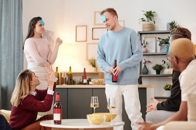 Groupe de jeunes amis interculturels joyeux dans des vêtements décontractés intelligents assis près d'une petite table ronde blanche dans le salon, prenant une pizza et des boissons