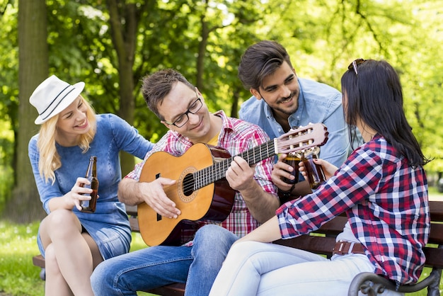 Groupe de jeunes amis jouant de la guitare et buvant de la bière sur un banc de parc