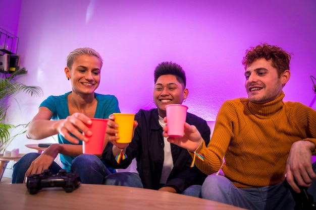 Groupe de jeunes amis jouant à des jeux vidéo ensemble sur le canapé à la maison portant un toast avec des lunettes jeunes millénaires