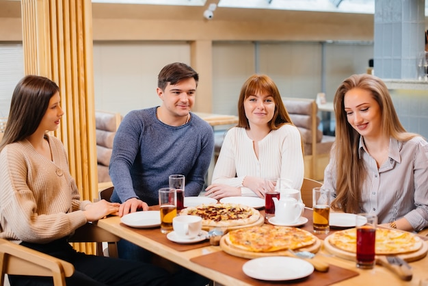 Un groupe de jeunes amis joyeux est assis dans un café à parler et à manger de la pizza