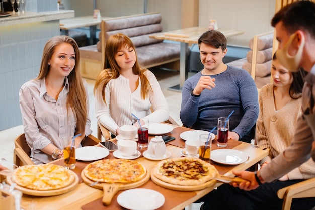 Un groupe de jeunes amis joyeux est assis dans un café en train de parler et de manger de la pizza