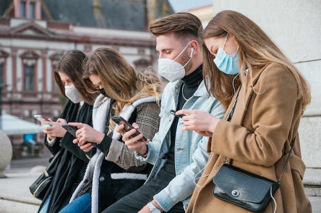 Groupe de jeunes amis portant un masque facial et utilisant leurs smartphones
