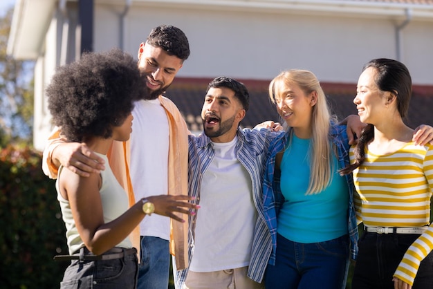 Un groupe de jeunes amis se tiennent ensemble à l'extérieur en souriant et en parlant.