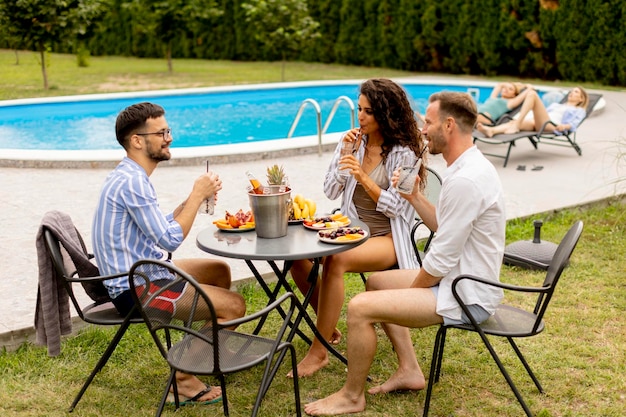 Groupe de jeunes applaudissant avec des boissons et mangeant des fruits au bord de la piscine dans le jardin