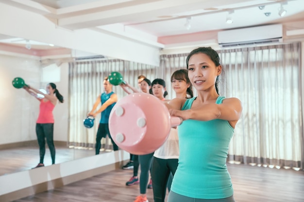 Groupe de jeunes athlètes masculins et féminins soulevant des kettlebells à l'intérieur dans une salle de sport. les sportifs qui s'entraînent avec une cloche de bouilloire ensemble des poids d'entraînement. les cours de club de sport attirent les amis s'entraînent ensemble.