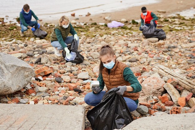 Groupe de jeunes bénévoles ramassant les ordures dans des sacs près de la côte à l'extérieur