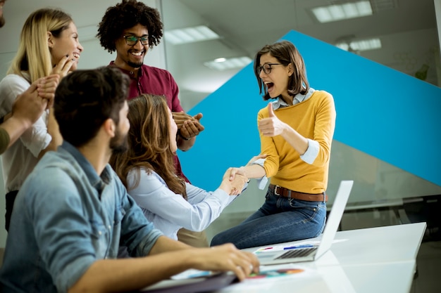 Groupe de jeunes collègues interagissant autour d&#39;une table et poignée de main au bureau