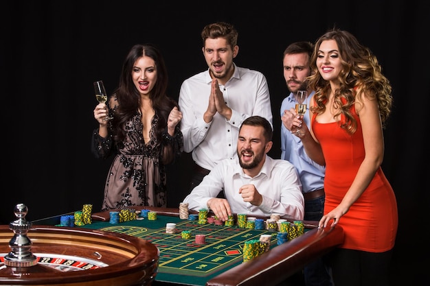 Groupe de jeunes derrière la table de roulette sur fond noir. Les jeunes ont fait des paris dans le jeu et attendent le résultat. Émotions vives