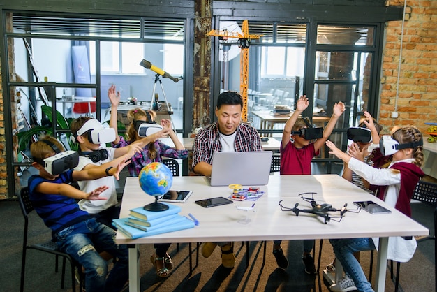 Groupe de jeunes élèves de l'école élémentaire à l'aide de lunettes de réalité virtuelle lors d'un cours de codage informatique.