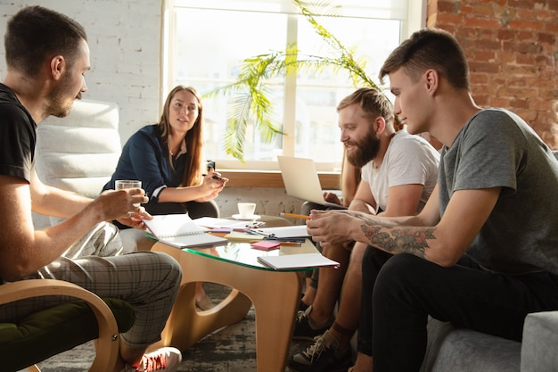 Groupe de jeunes employés de bureau caucasiens se réunissant pour discuter de nouvelles idées. Rencontre créative. Travail d'équipe et brainstorming. Les hommes et les femmes se réunissent au bureau pour planifier leur futur travail. Concept d'entreprise.