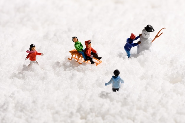 Groupe de jeunes enfants miniatures jouant en traîneau à neige ou en luge et la construction d'un bonhomme de neige