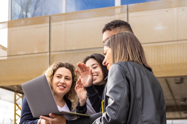 Groupe de jeunes entrepreneurs utilisant un ordinateur portable dans la rue Jeunes entrepreneurs passant un appel vidéo sur un ordinateur portable à l'extérieur