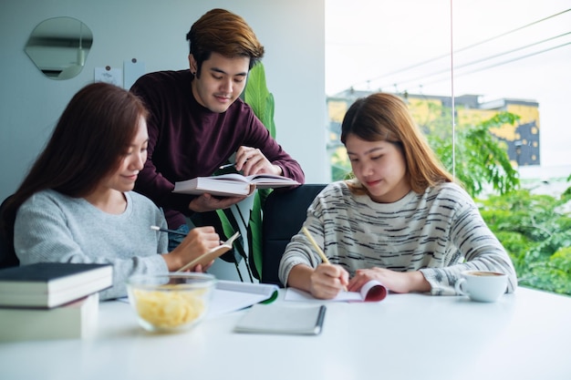 Groupe de jeunes étudiants faisant du tutorat et rattrapant le cahier d'exercices avec des amis