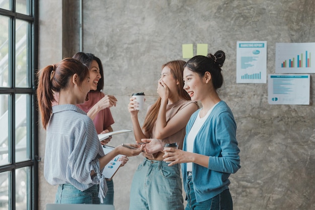 Un groupe de jeunes femmes d'affaires asiatiques se lèvent et parlent Ouvrir conjointement une entreprise en démarrage et un plan de gestion de plan d'affaires pour développer l'entreprise et être rentable par le concept de la nouvelle génération