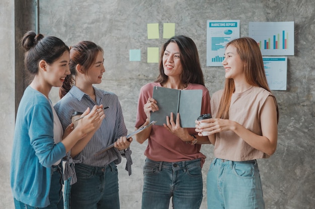 Un groupe de jeunes femmes d'affaires asiatiques se lèvent et parlent Ouvrir conjointement une entreprise en démarrage et un plan de gestion de plan d'affaires pour développer l'entreprise et être rentable par le concept de la nouvelle génération