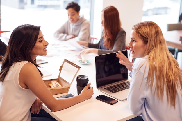 Groupe de jeunes femmes d'affaires assis autour d'une table dans un espace de travail moderne ayant un déjeuner de travail