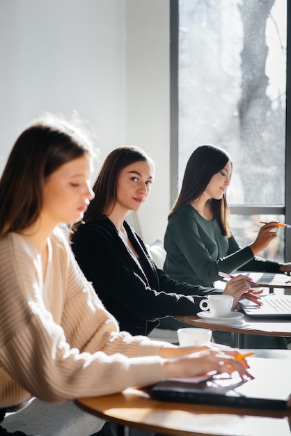 Un groupe de jeunes filles est assis dans un bureau devant des ordinateurs et discute de projets. Communication et formation en ligne.