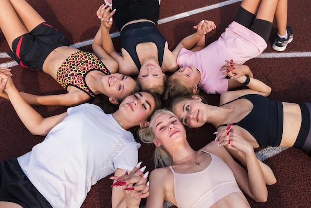 Groupe de jeunes filles en forme fatiguées et heureuses reposant sur le sol au stade