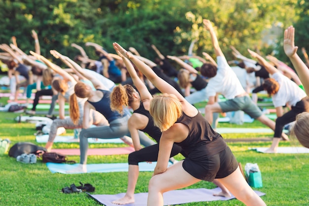 Un groupe de jeunes font du yoga dans le parc au coucher du soleil.