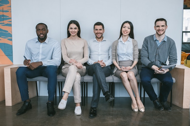 Groupe de jeunes gens d'affaires assis sur des chaises au bureau ensemble