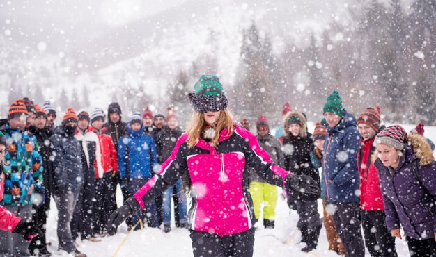 groupe de jeunes gens d'affaires heureux ayant une compétition de jeux les yeux bandés tout en profitant d'une journée d'hiver enneigée avec des flocons de neige autour d'eux lors d'un team building dans la forêt de montagne