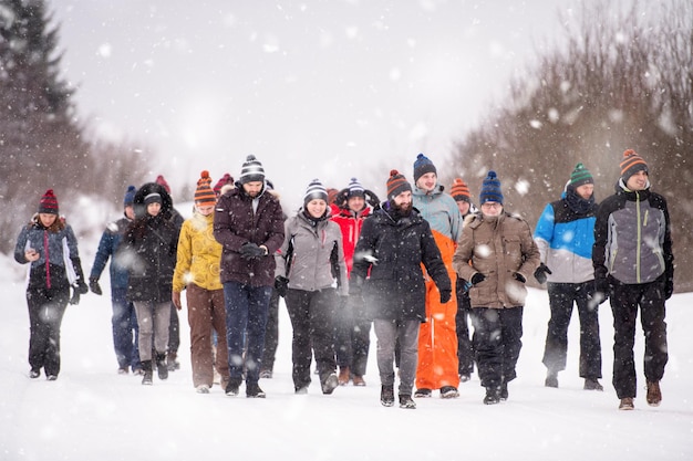 groupe de jeunes gens d'affaires marchant à travers un magnifique paysage d'hiver avec des flocons de neige autour d'eux lors d'un team building dans la forêt de montagne