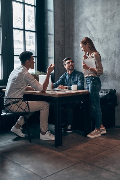 Groupe de jeunes gens modernes dans des vêtements décontractés intelligents discutant de quelque chose tout en travaillant au bureau