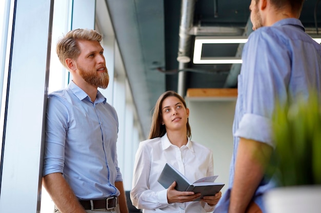 Groupe de jeunes gens modernes en tenue décontractée intelligente ayant une réunion de remue-méninges tout en se tenant dans le bureau de création